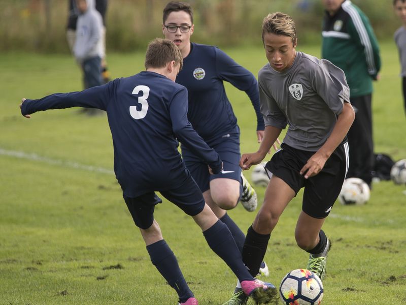 Three teenage boys playing a soccer match on a green field.