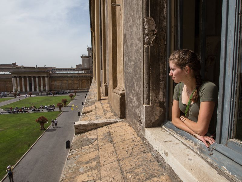 Teenage girl looking out a window at the Vatican Museums courtyard.