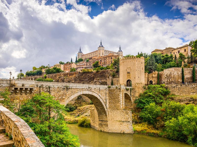 A view of the Alcazar of Toledo and the stone bridge crossing the river in Toledo, Spain.