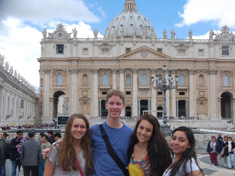 Four young adults stand together for a photo in front of St. Peter's Basilica in Vatican City.