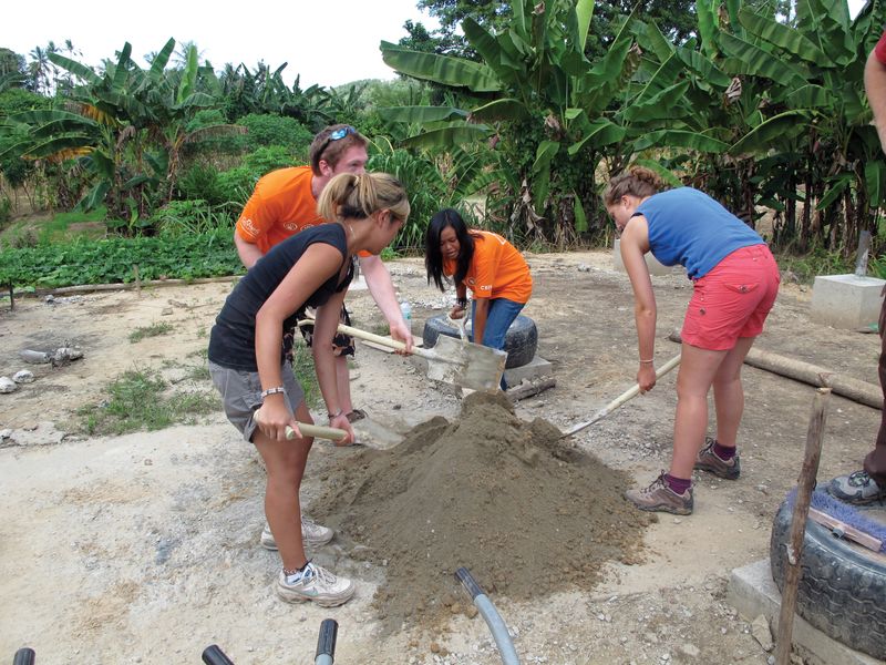 Young adults volunteering on a community building project, mixing cement and dirt with shovels.