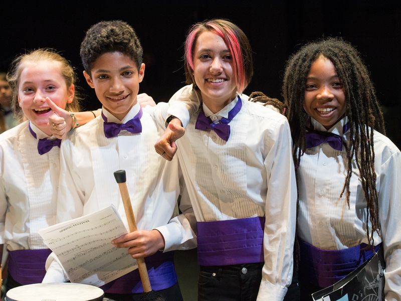 Four teenagers in concert attire smile at the camera