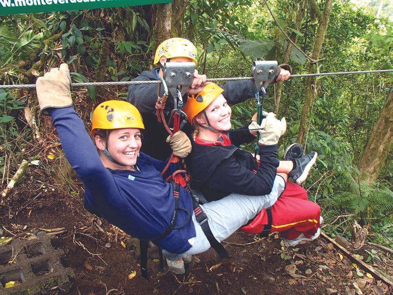 Three young adults ziplining through the rainforest in Monteverde, Costa Rica.