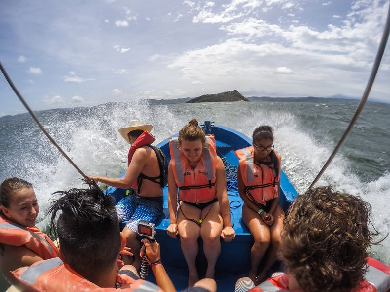 A group of people in a small boat, speeding through the ocean with large splashes of water around them.