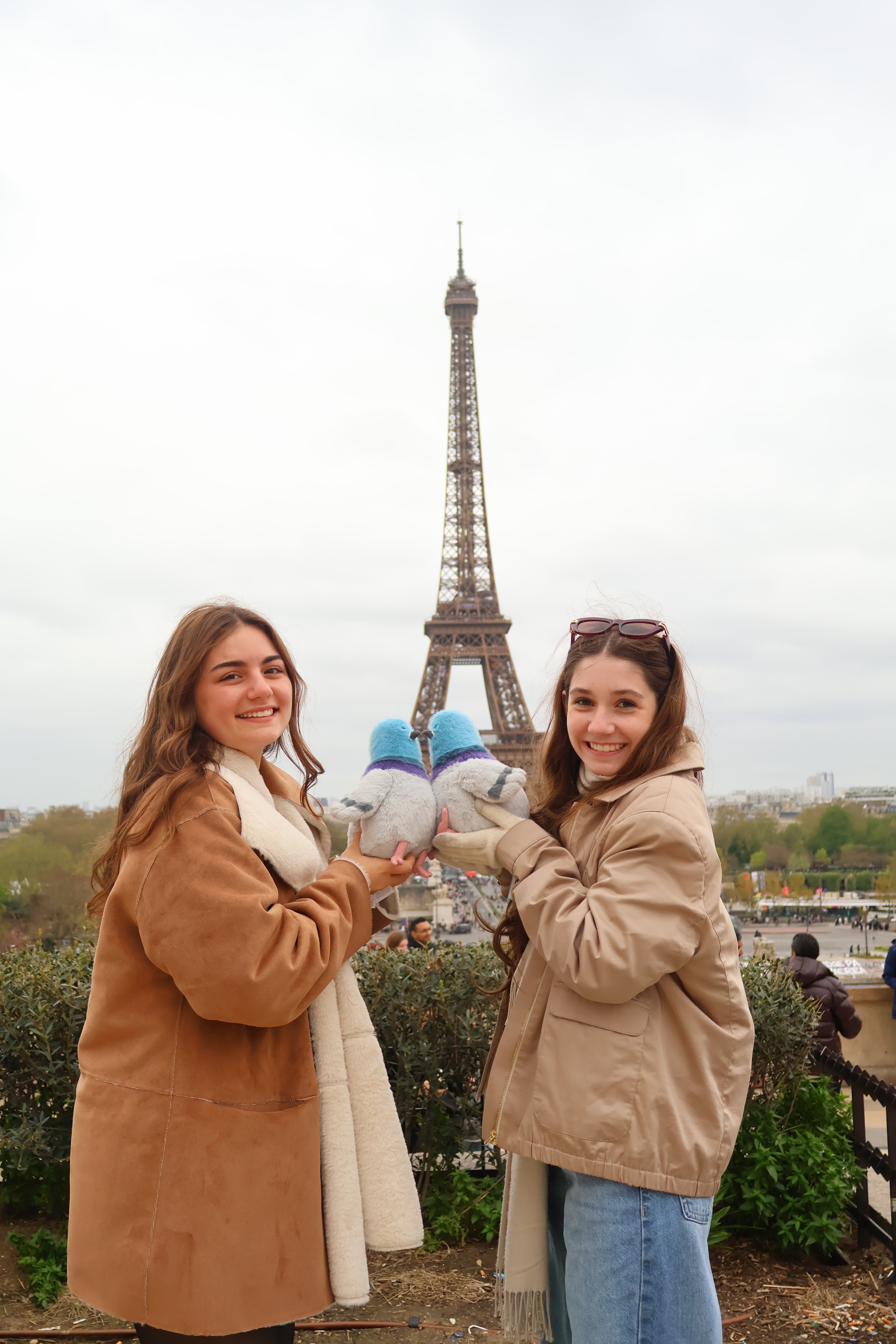 Two Young Women Posing with Pigeon Plushies in Front of the Eiffel Tower