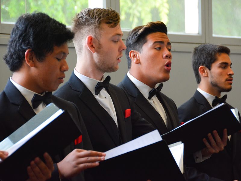 Four young men in tuxedos sing in a choir.