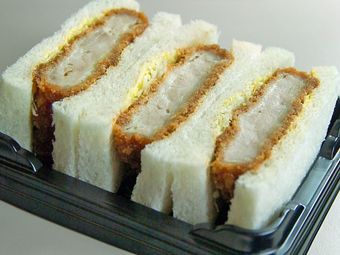 Close up of four halves of katsu sando in a black plastic to-go container