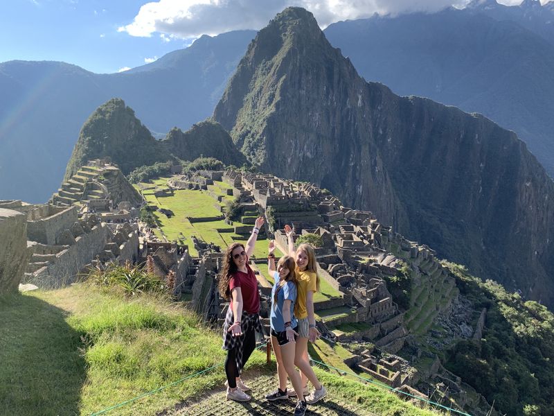 A group of people standing in front of Machu Picchu, with mountains in the background.