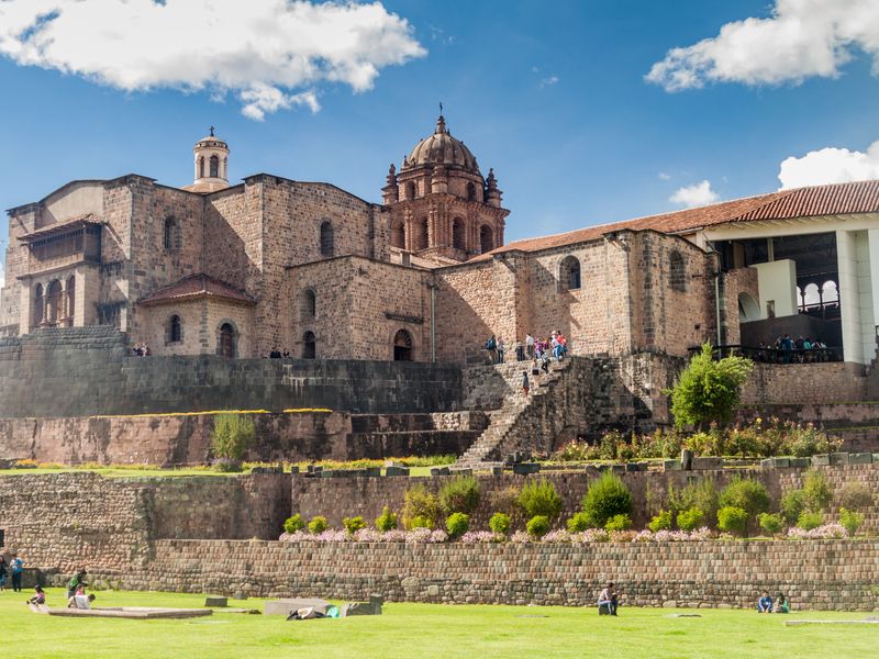 The Iglesia de la Compañía de Jesús in Cusco, Peru, is a Jesuit church built on the foundations of an Inca palace. It showcases a blend of Inca and Spanish colonial architecture. People can be seen exploring the site.