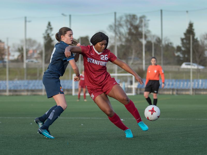 Action shot of two female soccer players competing for the ball during a game. The Stanford player is kicking the ball.