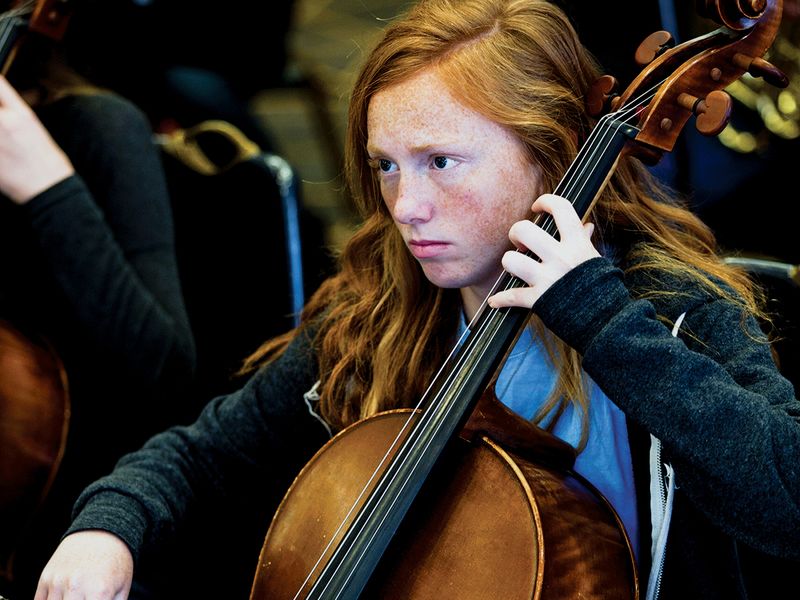 Teenage girl with red hair playing the cello in orchestra