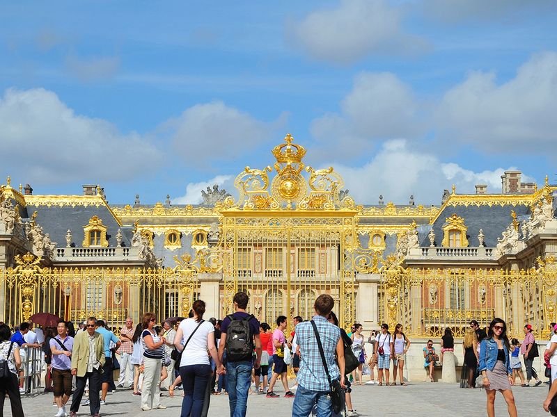 Crowd of tourists gather in front of the golden gates of the Palace of Versailles.