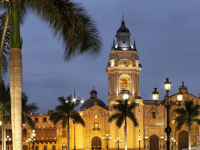 The Lima Cathedral illuminated at night, framed by palm trees in the Plaza Mayor, Lima, Peru.