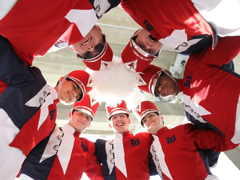 A marching band huddles together, looking down at the camera.