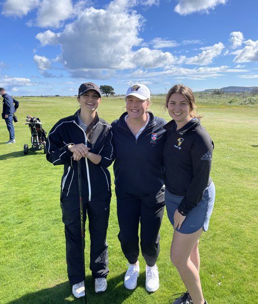 Three young women golfers stand together for a picture on a sunny golf course.