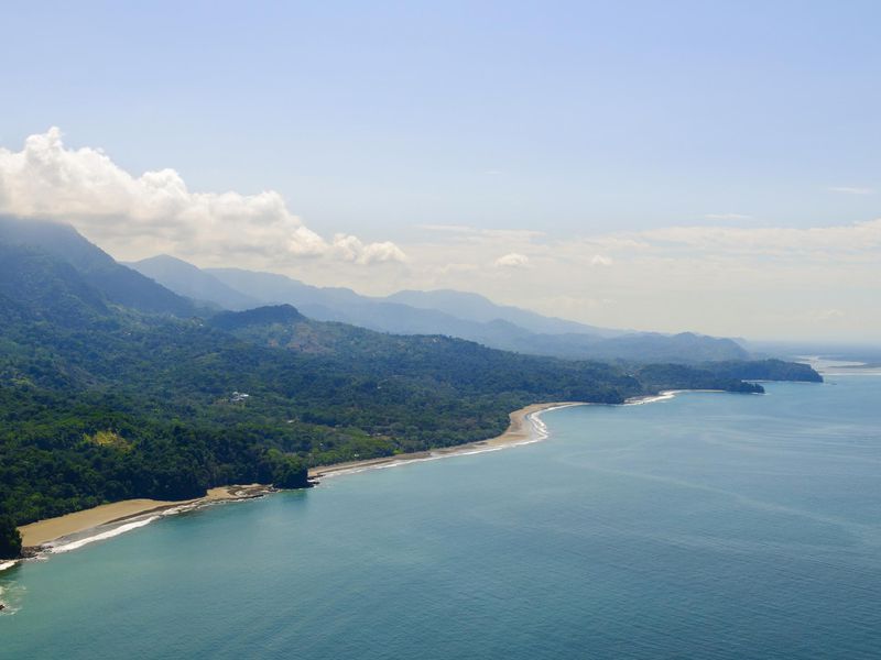 Aerial view of the Pacific Coast of Costa Rica, showcasing a stunning beach, verdant mountains, and clear blue waters.