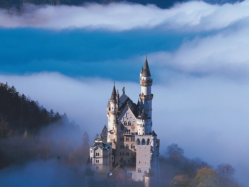 A majestic view of Neuschwanstein Castle perched on a hilltop, partially hidden by clouds.