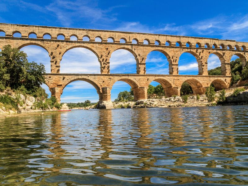 Pont du Gard Roman aqueduct bridge reflected in the Gardon River with kayakers.