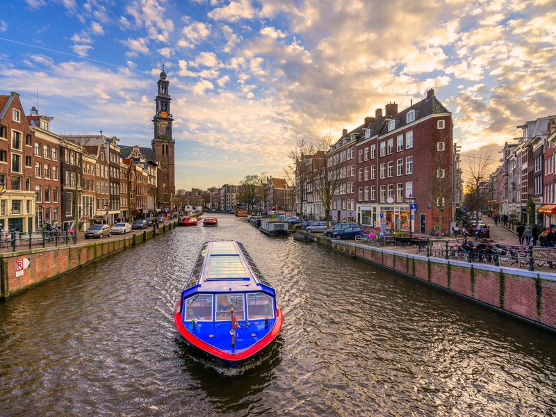 A canal boat navigates the waterways of Amsterdam at sunset, showcasing the city's charming architecture and vibrant atmosphere.