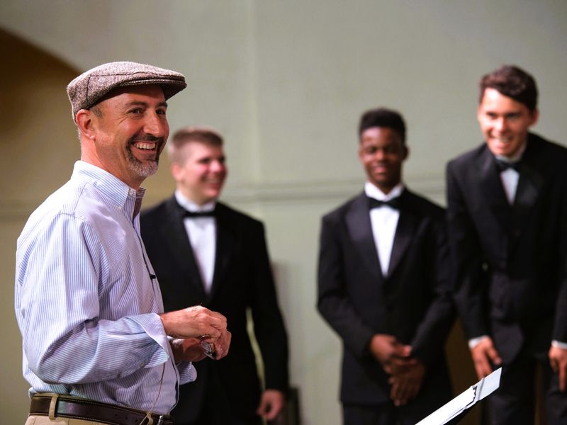 A group of men in formal wear, one conducting the others in a performance.